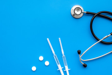 Medical examination and treatment concept. Stethoscope, syringe, pills on blue background top view copy space