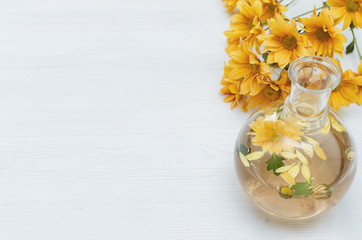 Chrysanthemum daisy flower essential oil tincture bottle on the white wooden table background with copy space. Herbal medicine.