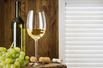 Wine bottle, glass of white wine and bunch of grapes on a old wooden barrel.