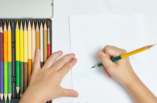 Kid Hands holds color pencil and think about drawing things on white blank paper on desk or study table