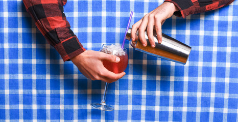 Male hands mixing drink or cocktail on checkered tablecloth