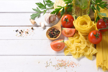 Dry pasta with vegetables on white wooden table.