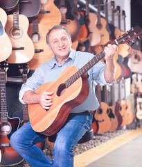 Adult guitarist is playing on acoustic guitar in music store.