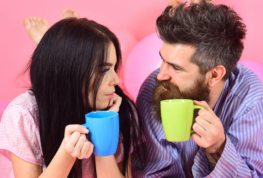 Couple relax in morning with coffee. Couple in love drink coffee in bed. Weekend morning concept. Man and woman in domestic clothes, pajamas. Man and woman on smiling faces lay, pink background.