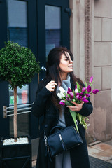Fototapeta premium Young girl walking on an old european city street with a bouquet of lilies in her hand
