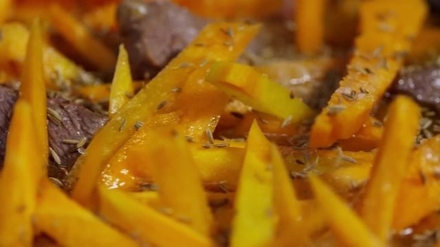 Extreme close up shot of red meat cubes and carrot sticks after frying, cook adding cumin to them, tracking left