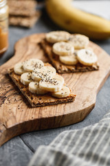 Two multi grain breads with peanut paste, banana slices and chia seeds on a serving wooden board. The concept of healthy fitness breakfast.