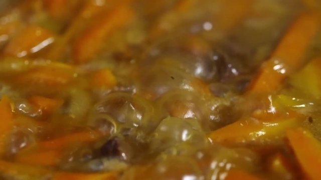 Close up shot of meat and carrots seasoned with cumin and coriander being braised in oil and water, tracking right