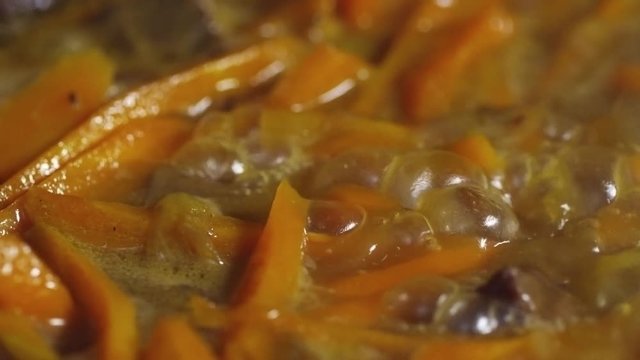 Close up shot of meat and carrots being braised in oil and water as part of pilaf preparation, tracking left