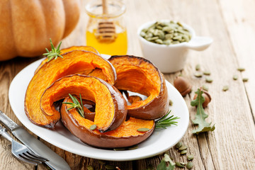 Baked pumpkin with rosemary and pumpkin seeds on wooden table. 