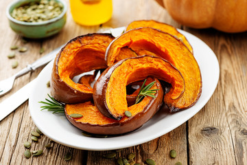 Baked pumpkin with rosemary and pumpkin seeds on wooden table. 