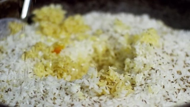 Close up shot of rice pilaf, cook sprinkling it with cumin seeds to put finishing touch to the dish