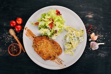 Fried schnitzel with potatoes and vegetables. Top view. On a wooden background. Copy space.