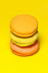 Delicious three multicolored macaroon on a yellow background