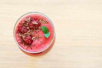 Raspberry smoothie in glass on light wooden table. Top view