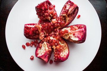 A red, ripe and juicy fruit of a round garnet lies alone on a round white plate.