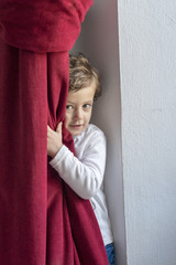 Child hiding behind a red curtain with smiling gesture