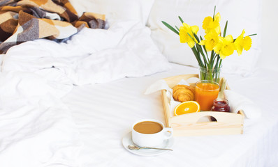 Morning breakfast in bed wooden tray with a cup of coffee croissant orange juice fresh orange jam bouquet of flowers daffodils. Top view Morning at Hotel Background Concept Interior Copy Space