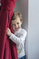 Child hiding behind a red curtain with smiling gesture
