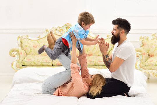 Mother and father cuddling with cute son. Young family spend time together on bed, luxury interior background. Parents with happy faces pay attention to kid, play, have fun. Happy family concept.
