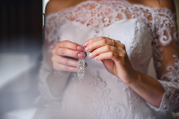 bride holding Bridal silver earrings in her hands on white dress background with French manicure close-up