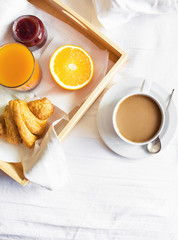 Morning breakfast in bed wooden tray with a cup of coffee croissant orange juice fresh orange jam Bed linen. Top view Hotel Room Early Morning at Hotel Background Concept Interior Copy Space