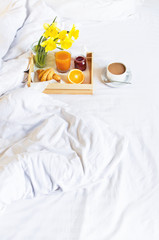 Morning breakfast in bed wooden tray with a cup of coffee croissant orange juice fresh orange jam bouquet of flowers daffodils. Top view Morning at Hotel Background Concept Interior Copy Space