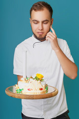 young male confectioner in a tunic with cake in the studio