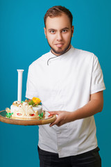 young male confectioner in a tunic with cake in the studio