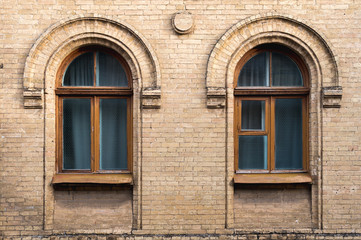 Fototapeta na wymiar Two vintage arched windows in a wall of yellow bricks. Green - the colors of sea wave glass in a maroon dark red wooden frame. The concept of antique vintage architecture in building elements