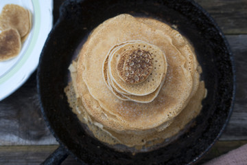 Large and small pancakes are placed in a frying pan on an old wooden table.