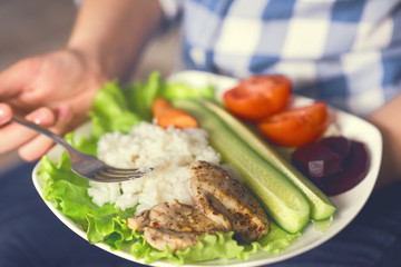 A girl holds a plate with vegetables and chicken meat with spices. Healthy eating concept. Girl in jeans and a plaid shirt. Proper nutrition. Diet. Health. Chicken meat with spices. Small depth of