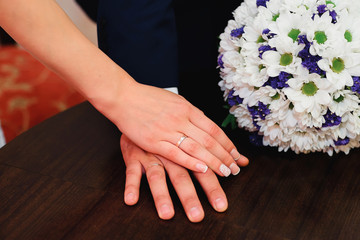 hands of bride and groom with rings on wedding bouquet background