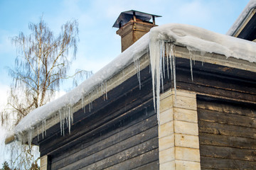 Icicles on the edge of the roof of a wooden house in winter
