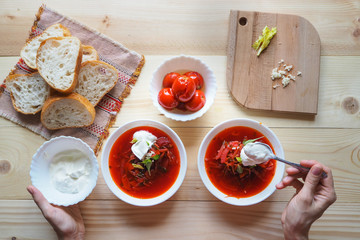 Fototapeta na wymiar The addition of sour cream in the soup. Ukrainian traditional borsch. Russian vegetarian red soup in white bowl on wooden background. Top view.