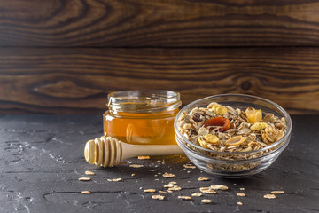 Muesli with dried apricots and granola, fresh honey in glass plate on wooden background. Healthy...