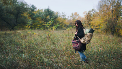 A girl in a coat with a backpack in an autumn forest stands in profile. Camping concept.