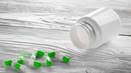 Medical green pills and white bottle on wooden background.