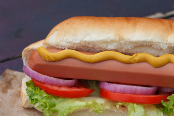 Hot dog with mustard, lettuce, tomato and onions. Fast food.