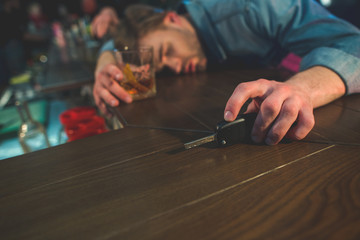 Drunk driver sleeping on counter. He holding key in hand. He locating in bar
