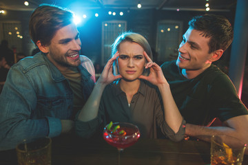 Portrait of frustrated woman feeling headache while listening conversation of two molesting males....