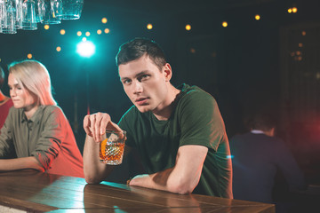 Portrait of concentrated young man drinking glass of whiskey at counter. Relax in bar concept