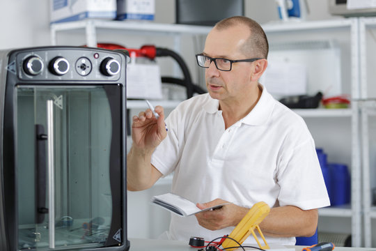 repairman with screwdriver fixing oven in kitchen