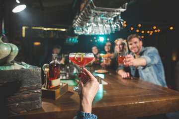 Close up female hand keeping cocktail. Comrades situating opposite her at counter. Leisure in club concept