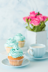 Blue pastel vertical banner with decorated cupcakes, cup of coffe with milk and bouquet of pink roses.