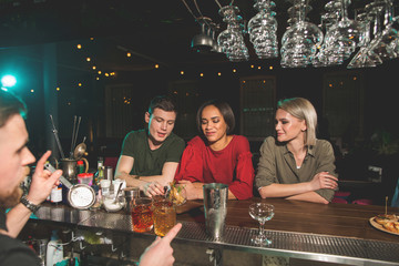 Outgoing man talking with two happy girls. They drinking cocktails while sitting in nightclub. Cheerful clients telling during rest concept