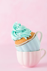 Cupcake with gentle blue cream decoration in two cups on pink pastel background.