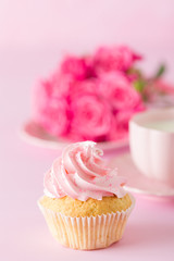 Cupcake with pink cream decoration and roses on pink pastel background.