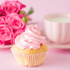 Cupcake with pink cream decoration and roses on pink pastel background.
