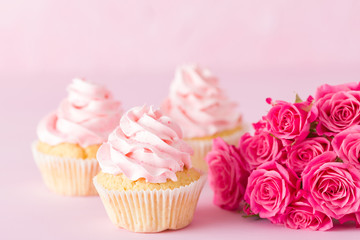 Cupcake with pink cream decoration and roses on pink pastel background.
